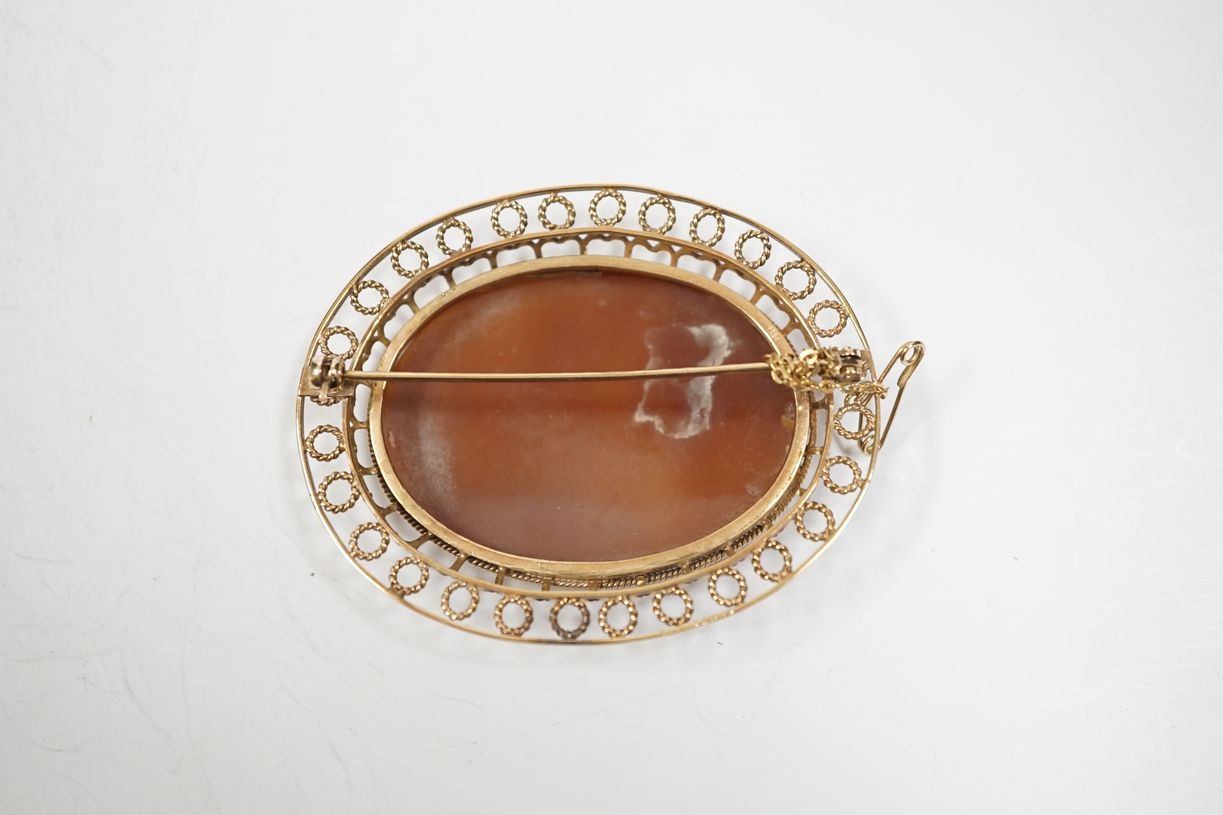 A yellow metal mounted oval cameo shell brooch, carved with two seated ladies with sheep, beneath a tree, 61mm, gross weight 19.9 grams.